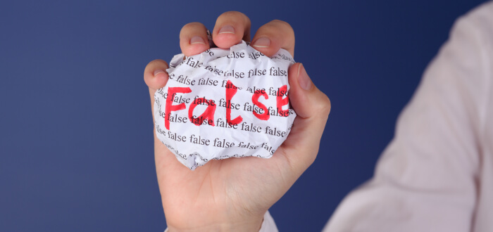 Person holding up crumpled paper that says false