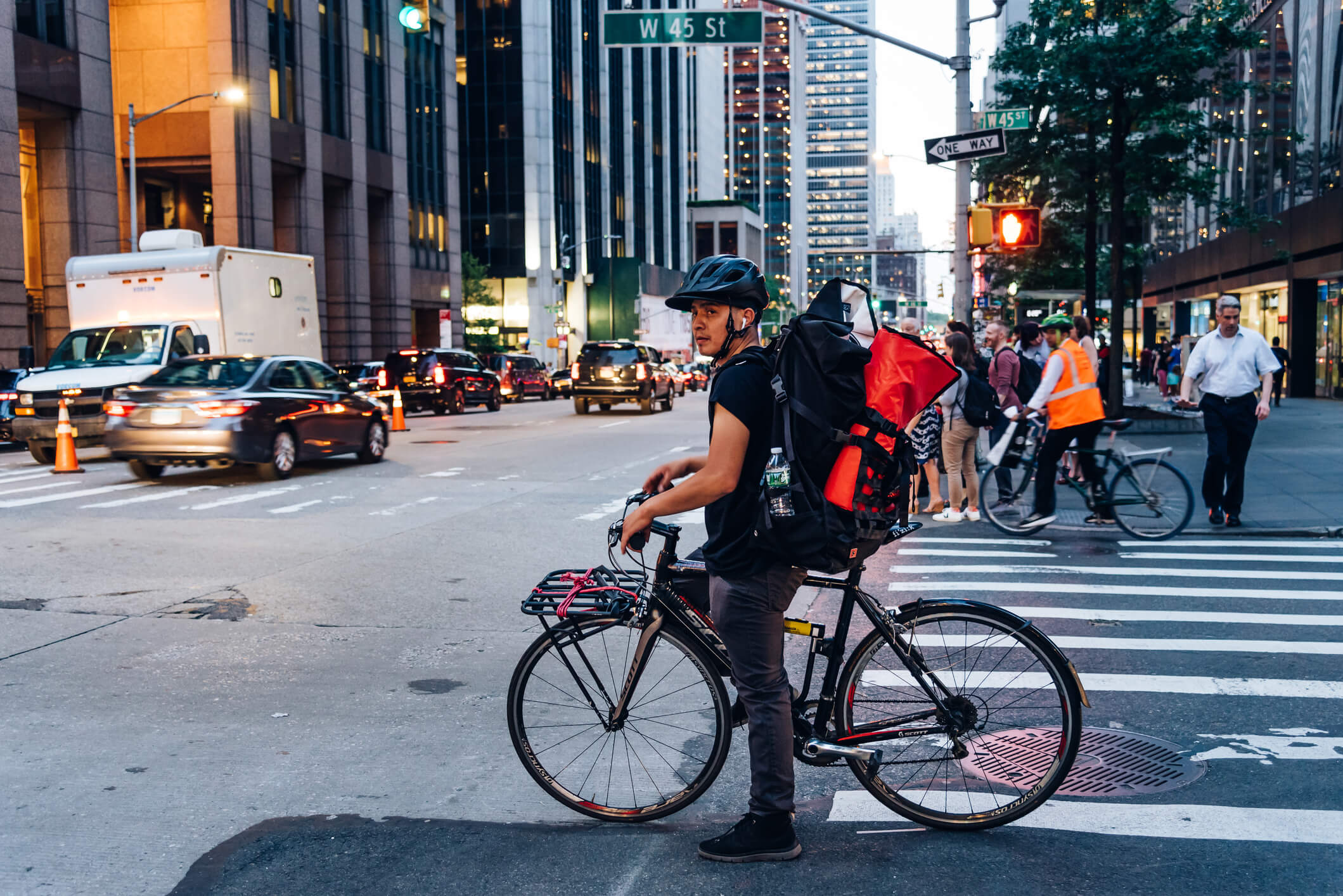 New York City, USA - June 21, 2018: Hispanic courier on bicycle in crosswalk in New York City at dusk